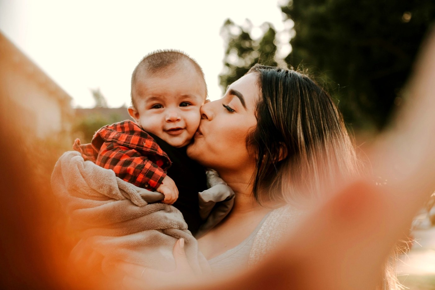 Una madre besa a su bebé en la mejilla, luz cálida de atardecer